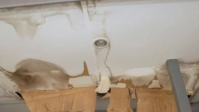 Sagging water-damaged ceiling drywall with torn paper and a pipe fitting above